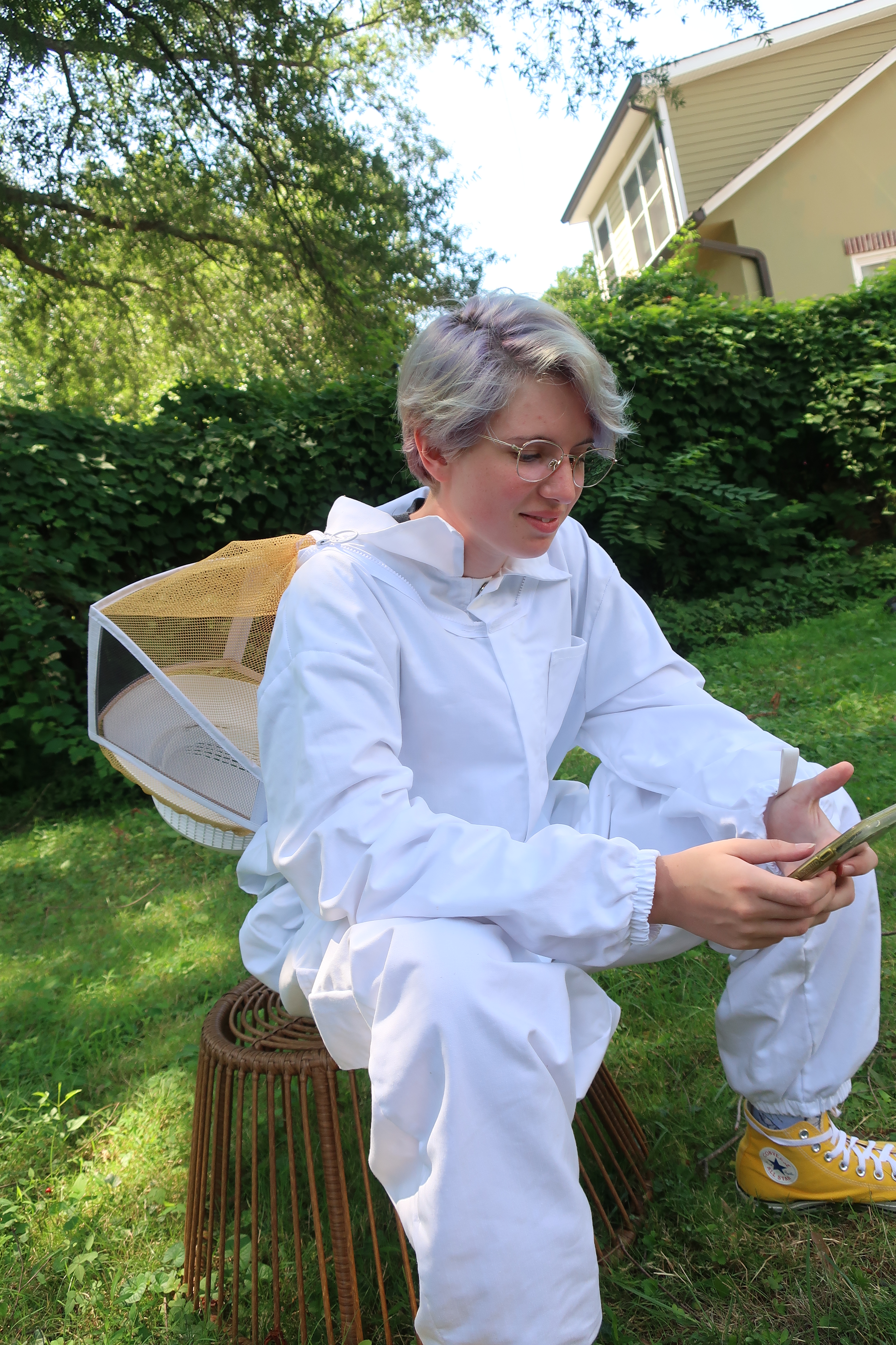 Queen Beekeeper Nicki seated outdoors in a white beekeeping suit